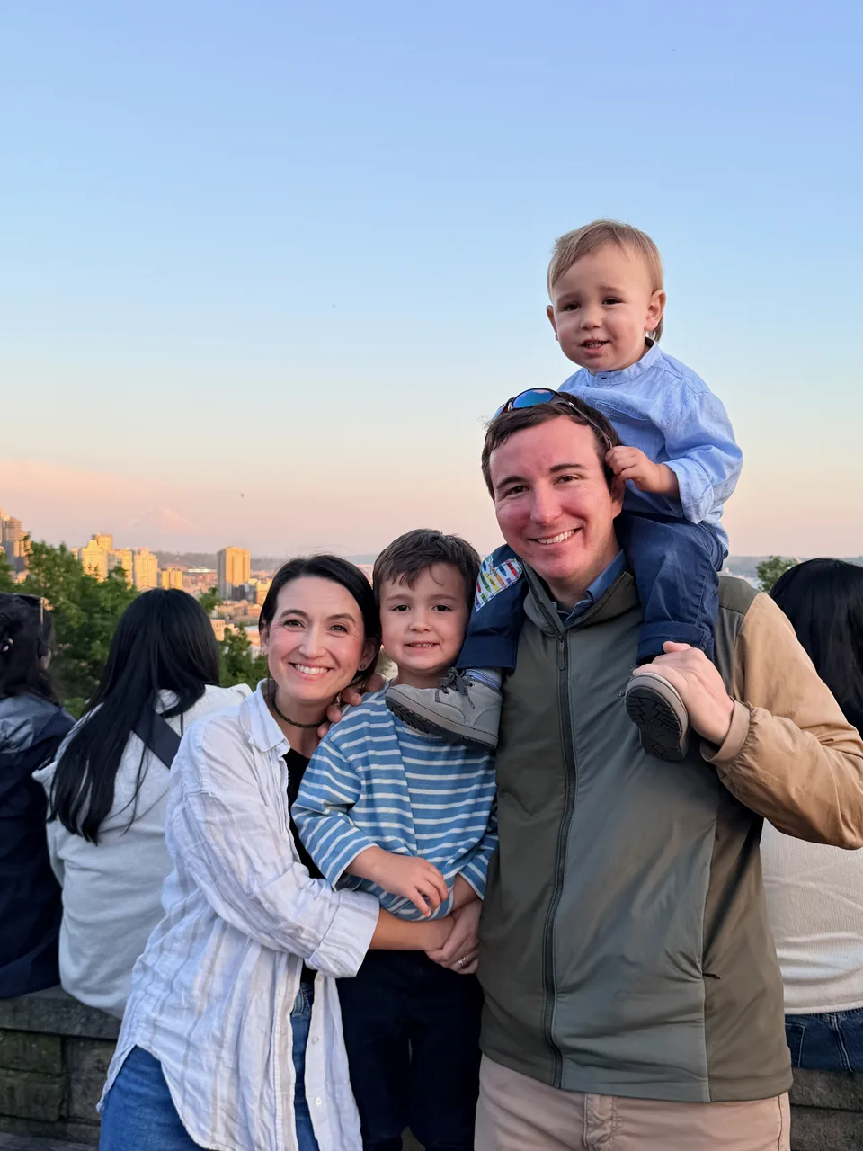 A family of four together outdoors beneath a pastel evening sky